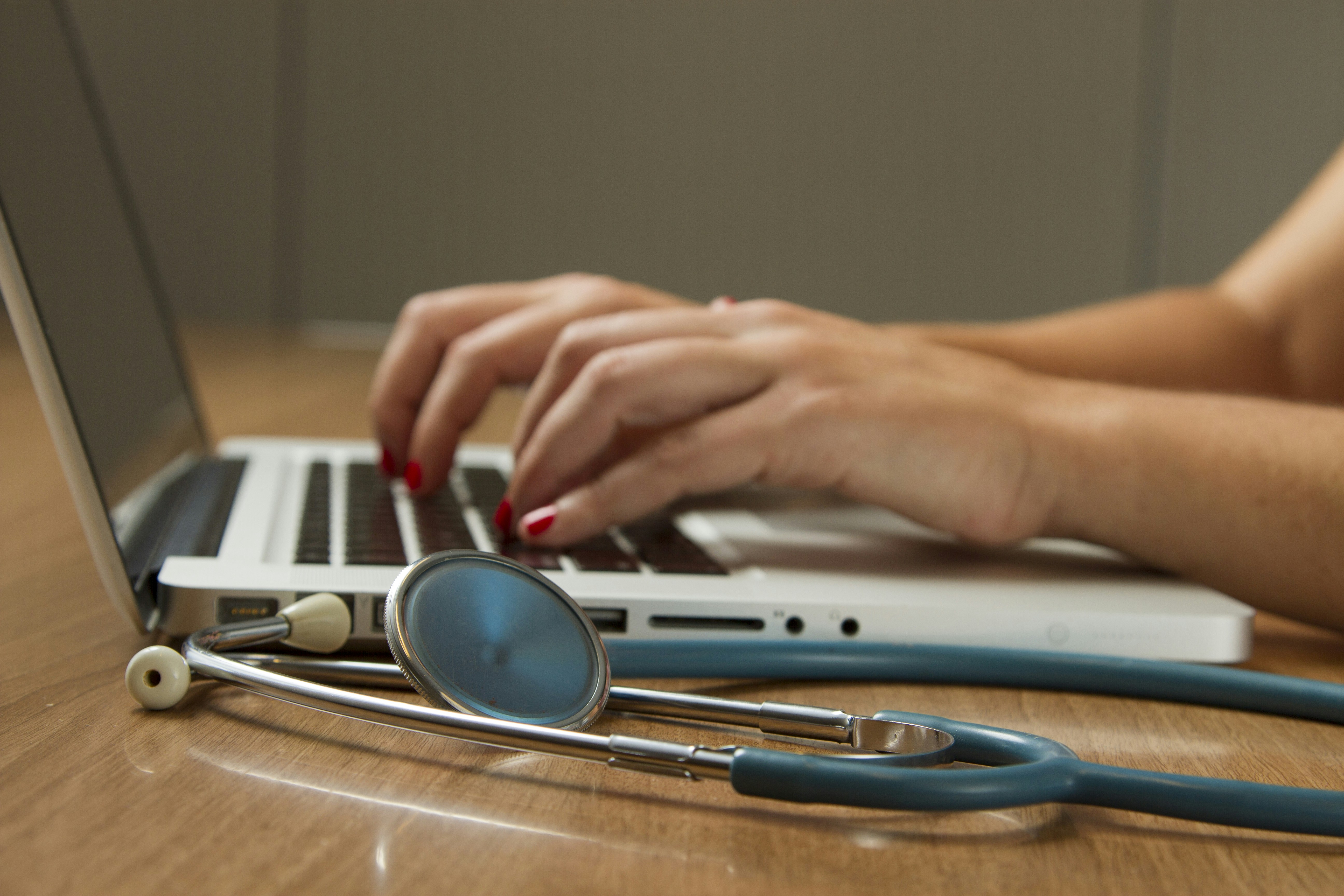 hands typing on laptop with stethoscope nearby - Discover how the right custom healthcare software development company can enhance patient care and meet industry standards. Learn more now!ith 
